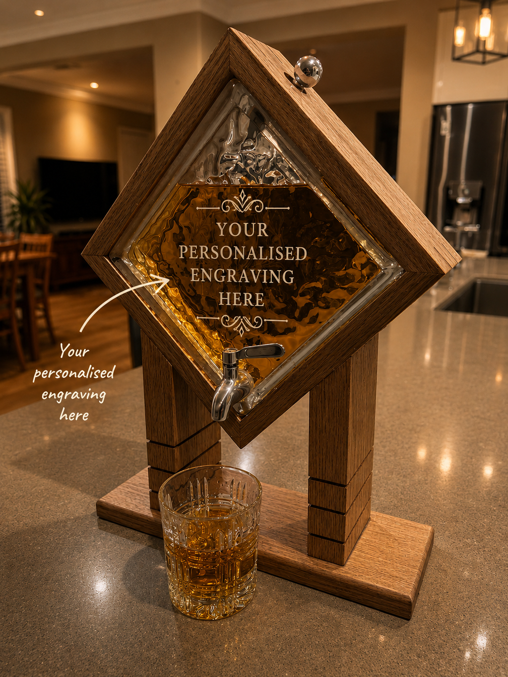 A diamond-shaped wooden whiskey dispenser with a clear glass front panel and metal tap, shown on a kitchen counter with a glass of amber liquid. The front has sample personalized engraving text and an arrow pointing to it.