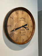 Wine barrel wall clock made from reclaimed oak barrel head with Roman numerals and black metal hands mounted on wall.