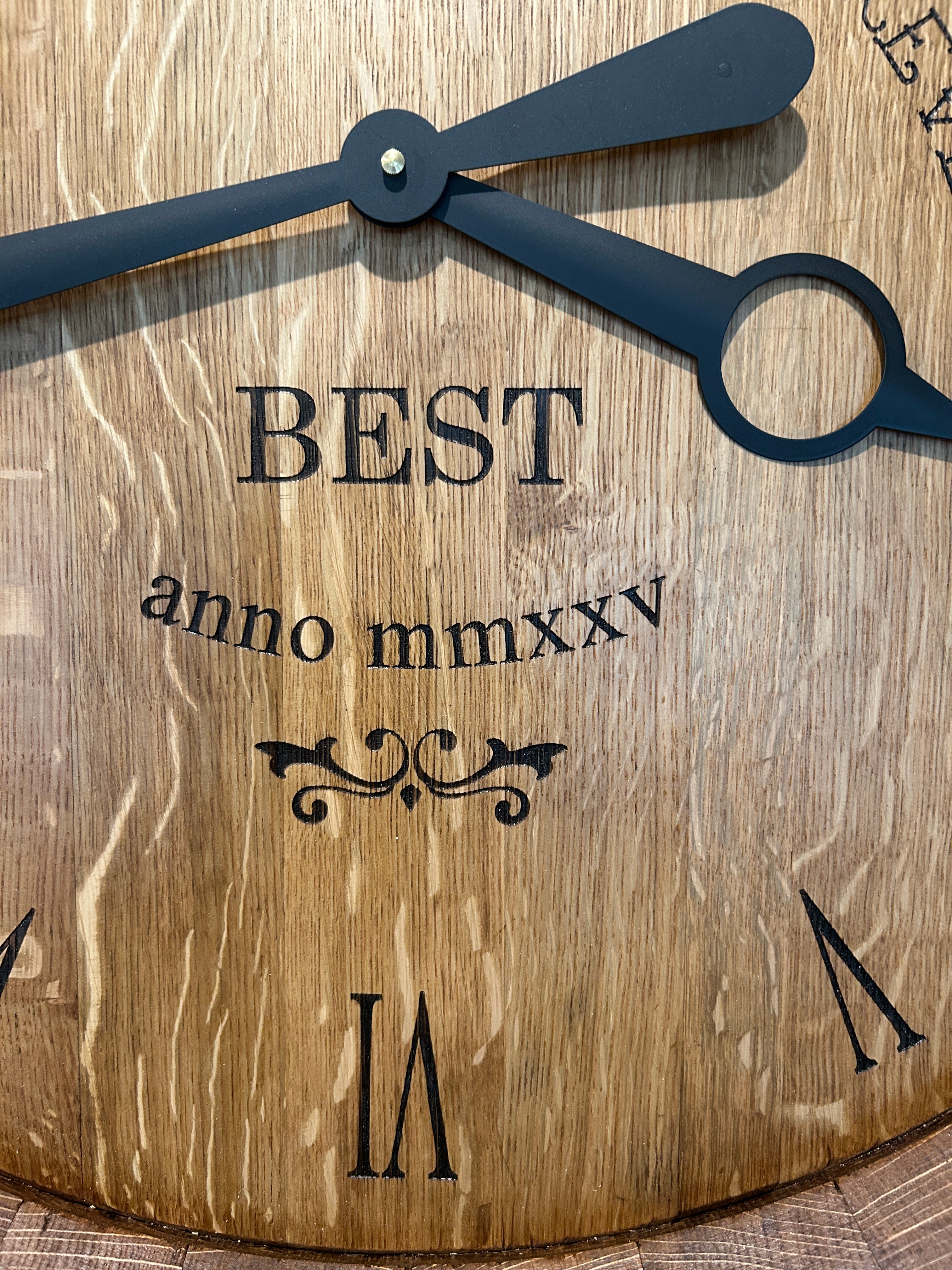 Close-up of engraved wine barrel clock face showing Roman numerals and black metal hands on reclaimed oak barrel head.
