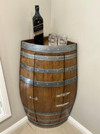 Corner wine barrel bar in natural oak with a bottle and glasses on top against a plain wall.