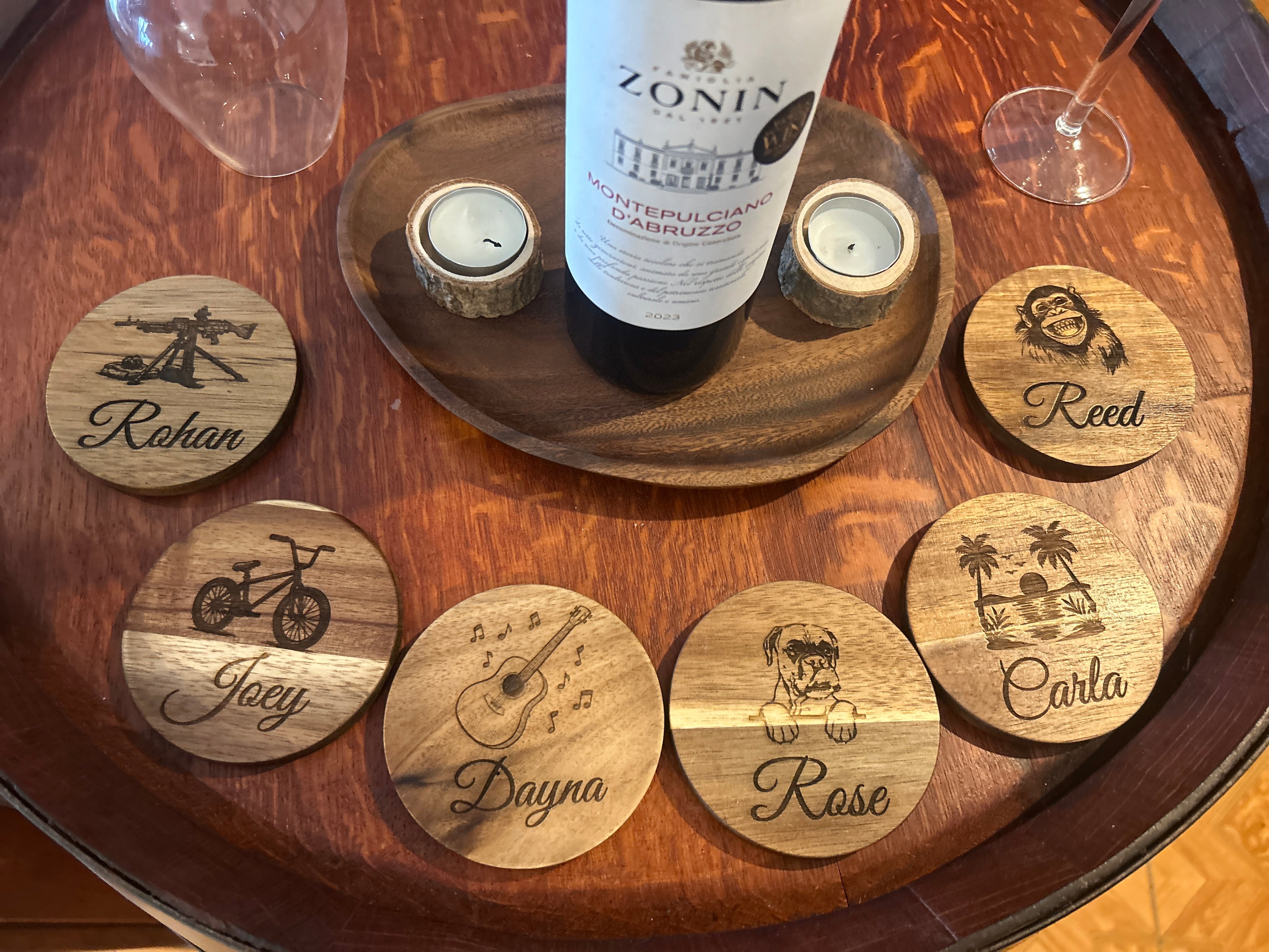Wooden coasters with engraved names on a wooden tray with a bottle of wine and glasses.