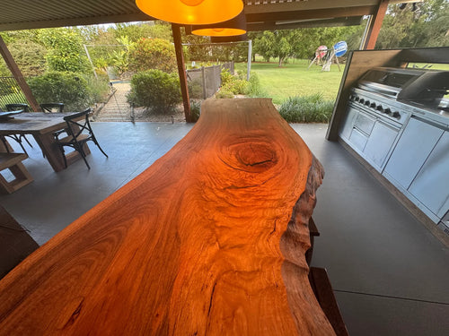 Spotted Gum live edge slab in an outdoor setting with a grill and patio furniture in the background.